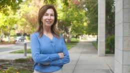 Julie Gallelo, standing outside in a blue blouse with hwr arms crossed and smiling towards the camera