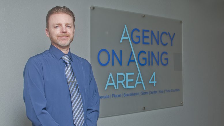 Man in a dress shirt and tie standing in front of a Agency on Aging Area 4 sign.
