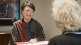 Woman sitting at desk talking to someone sitting across from their desk.