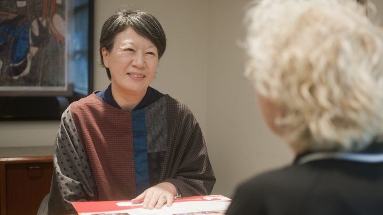 Woman sitting at desk talking to someone sitting across from their desk.