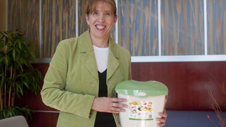 Carrie Whitlock stand and smiles for the camera holding a home organic waste bin