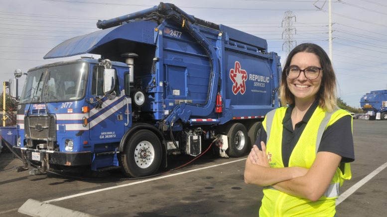 Annah Rulon in a high visibility vest standing in front of a waste vehicle